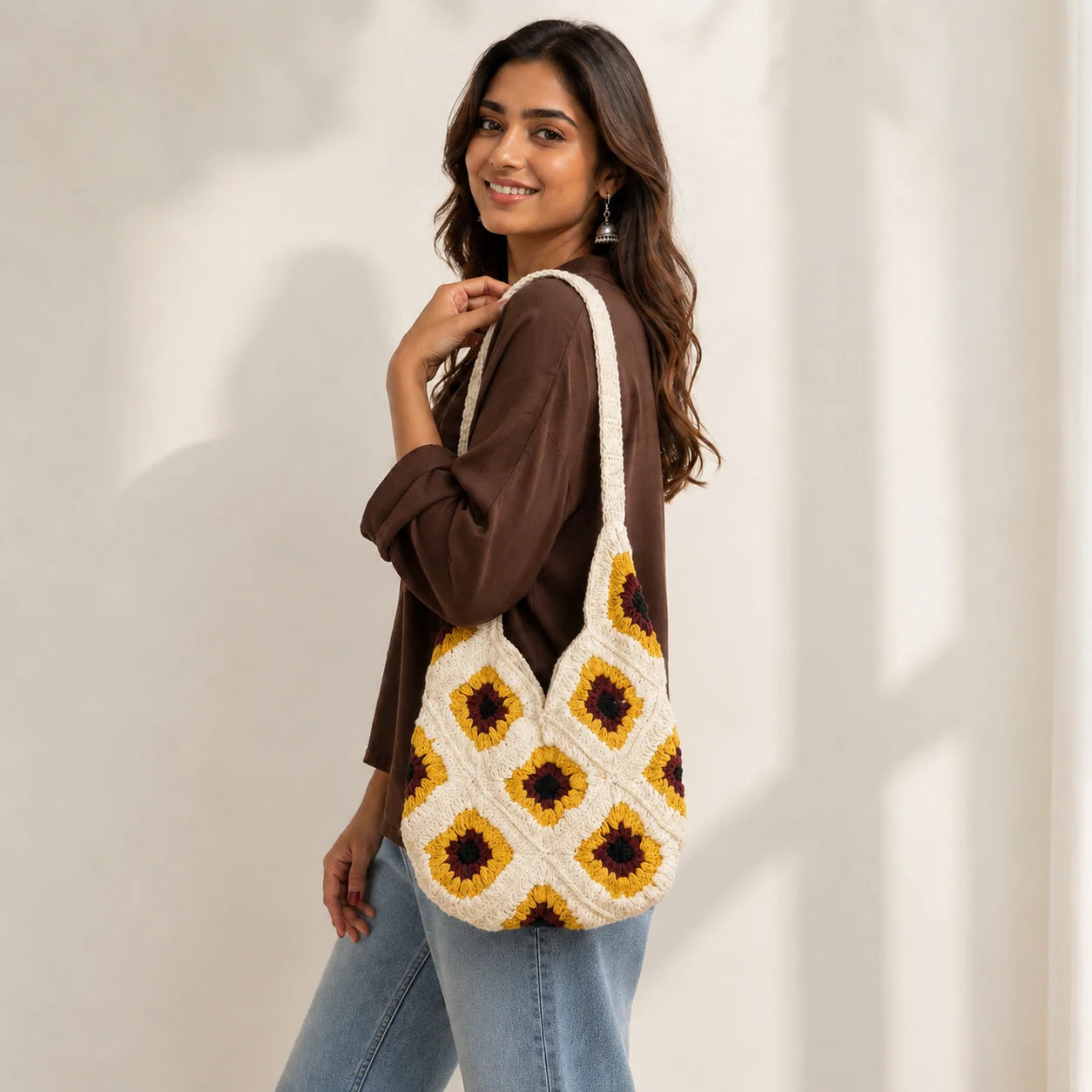 "White crochet bag with
 mustard yellow and brown floral motifs, featuring a textured geometric pattern and a long crochet shoulder strap."
