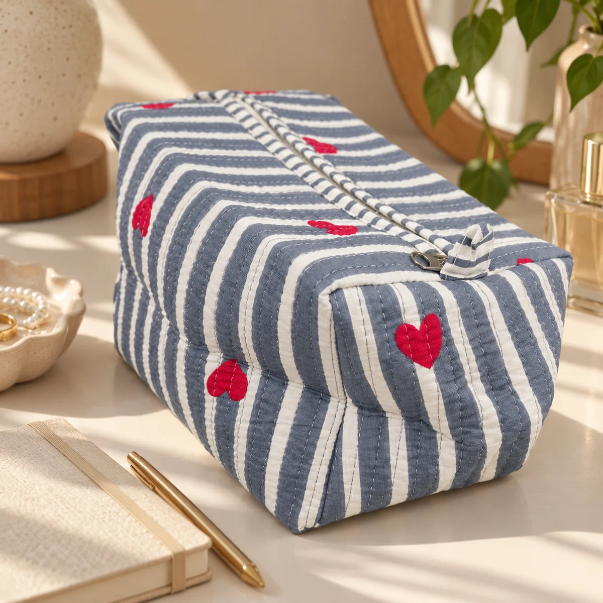 "Quilted blue and white
 striped pouch featuring small red heart motifs, a structured rectangular shape, and a top closure."
