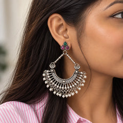"Oxidised silver-tone
 chandbali earrings with intricate detailing, colourful stone accents, and cascading pearl-like bead drops."
