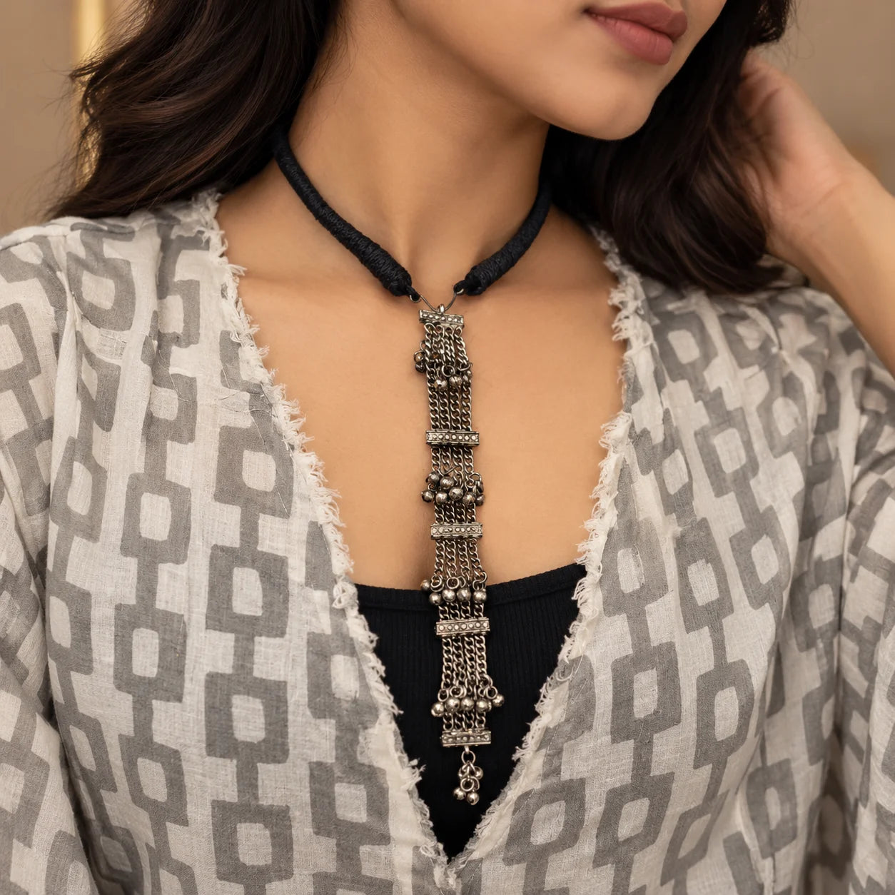 " Oxidised silver-tone 
necklace with a black braided thread and long cascading chain strands decorated with intricate metalwork and small dangling silver beads."
