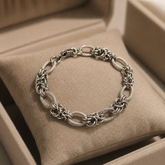 Demi-fine 925 silver plated chain bracelet for women with lobster clasp. Chunky woven textured link design with polished finish on wooden table. Silver tone anti-tarnish wrist bracelet with secure closure for daily wear.
