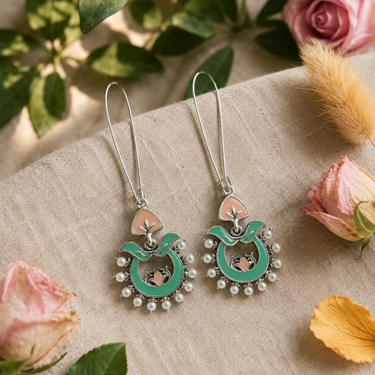 These traditional enamel hoop earrings feature hand-painted turquoise enamel work, delicate pink lotus detailing, and a halo of pearl beads on an silver chandbali frame. The wire hook design keeps them lightweight for all-day wear, while the vibrant enamel adds a festive pop to ethnic and indo-western outfits. Each piece reflects classic Indian craftsmanship with a modern boho twist.
