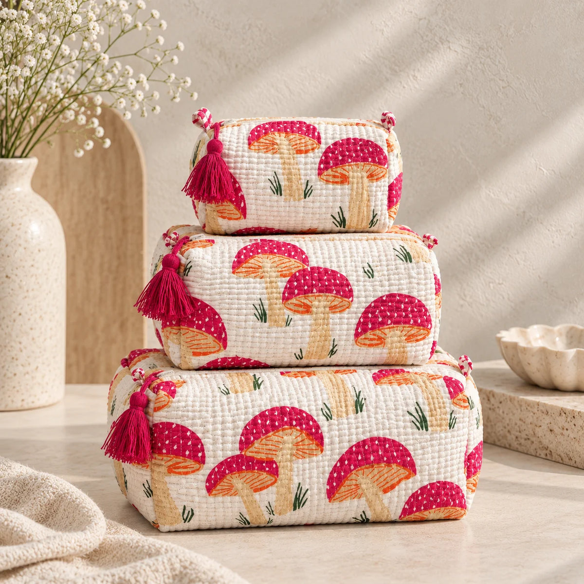 Set of three white quilted cotton toiletry bags with pink mushroom print stacked together

