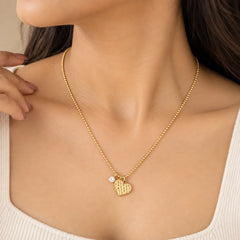 "Delicate gold-tone necklace 
featuring a textured heart-shaped pendant and a small sparkling stone accent on a fine chain."
