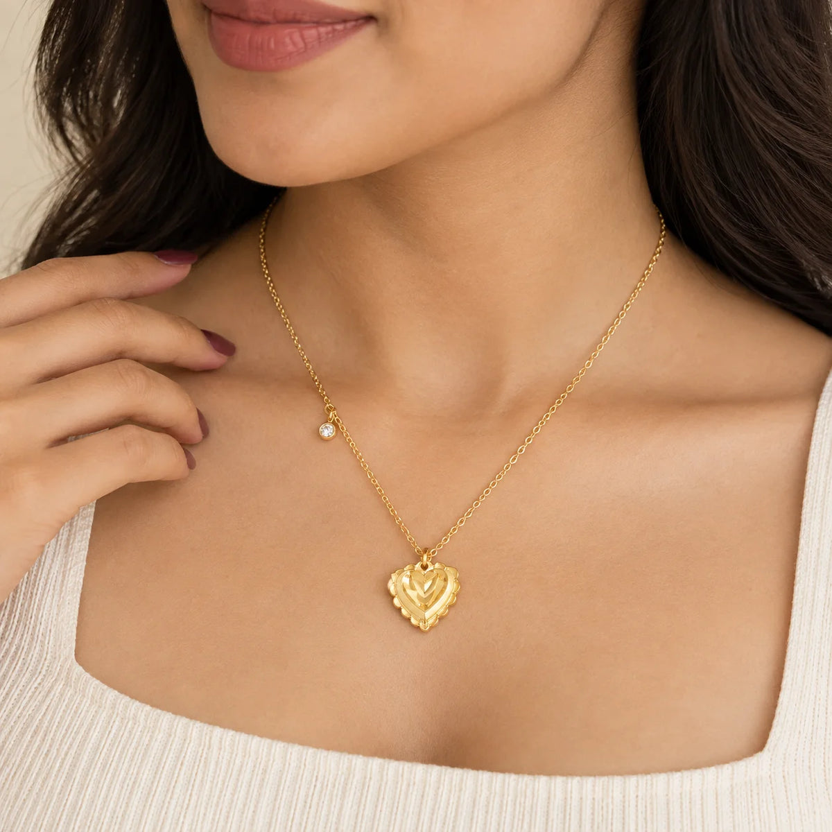 "Gold-tone necklace with
 a delicate chain, featuring a textured heart-shaped pendant and a small sparkling crystal charm, displayed on a dark laptop surface."
