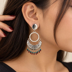"Silver-tone 
 earrings with layered circular hoops, intricate textured detailing, and colourful red and turquoise bead drops."
