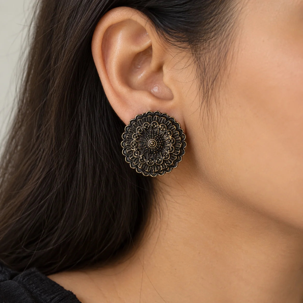 "Pair of oxidised silver-tone 
statement earrings featuring intricate circular mandala-inspired floral patterns with layered ornamental detailing, displayed on a white jewellery card."

