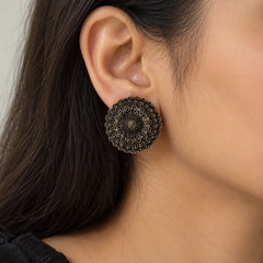 "Pair of oxidised silver-tone 
statement earrings featuring intricate circular mandala-inspired floral patterns with layered ornamental detailing, displayed on a white jewellery card."
