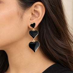 "Gold-tone statement 
earrings featuring three glossy black heart-shaped charms arranged in a cascading  design."
