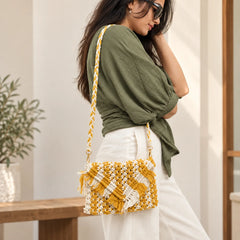 "Mustard and white
macramé bag featuring an intricate woven pattern, layered fringe detailing, and a braided shoulder strap."

