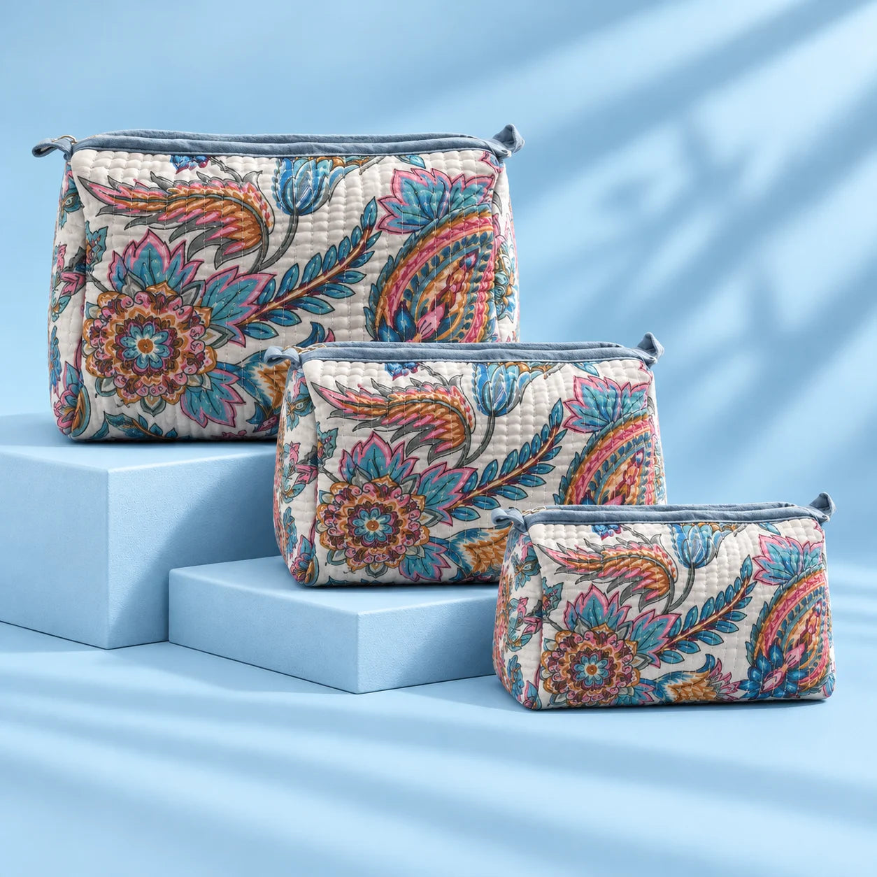 "Quilted fabric bag with a 
soft white base, featuring vibrant blue, pink,  mustard and earthy floral prints, with a structured  shape and top handle."
