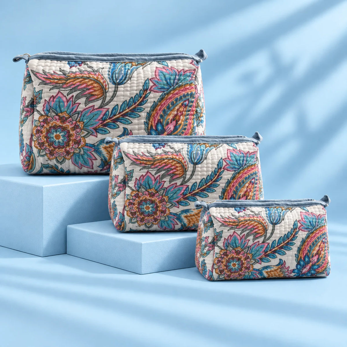 "Quilted fabric bag with a 
soft white base, featuring vibrant blue, pink,  mustard and earthy floral prints, with a structured  shape and top handle."
