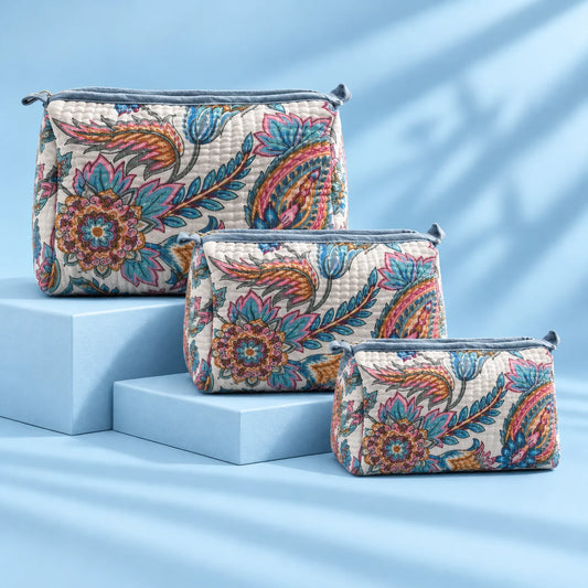 "Quilted fabric bag with a 
soft white base, featuring vibrant blue, pink,  mustard and earthy floral prints, with a structured  shape and top handle."
