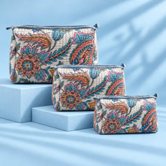 "Quilted fabric bag with a 
soft white base, featuring vibrant blue, pink,  mustard and earthy floral prints, with a structured  shape and top handle."
