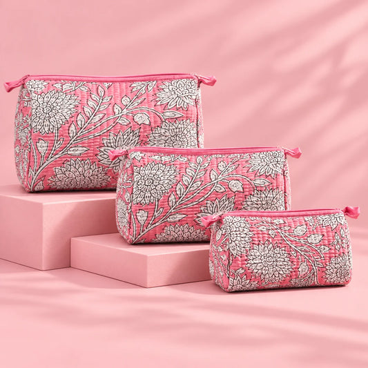 "Set of three pink quilted
 fabric pouches featuring intricate white floral and botanical prints, arranged in different sizes."

