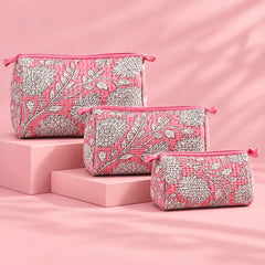 "Set of three pink quilted
 fabric pouches featuring intricate white floral and botanical prints, arranged in different sizes."
