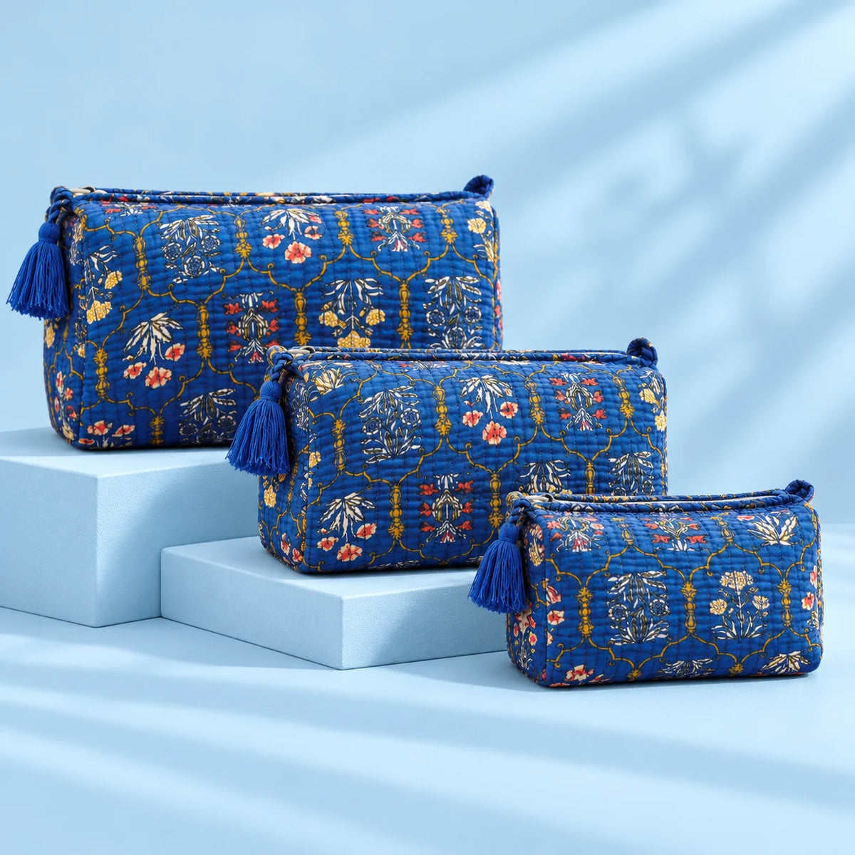 "Set of three royal blue
 quilted fabric pouches featuring intricate floral and ornamental prints with tassel details and arranged in different sizes."
