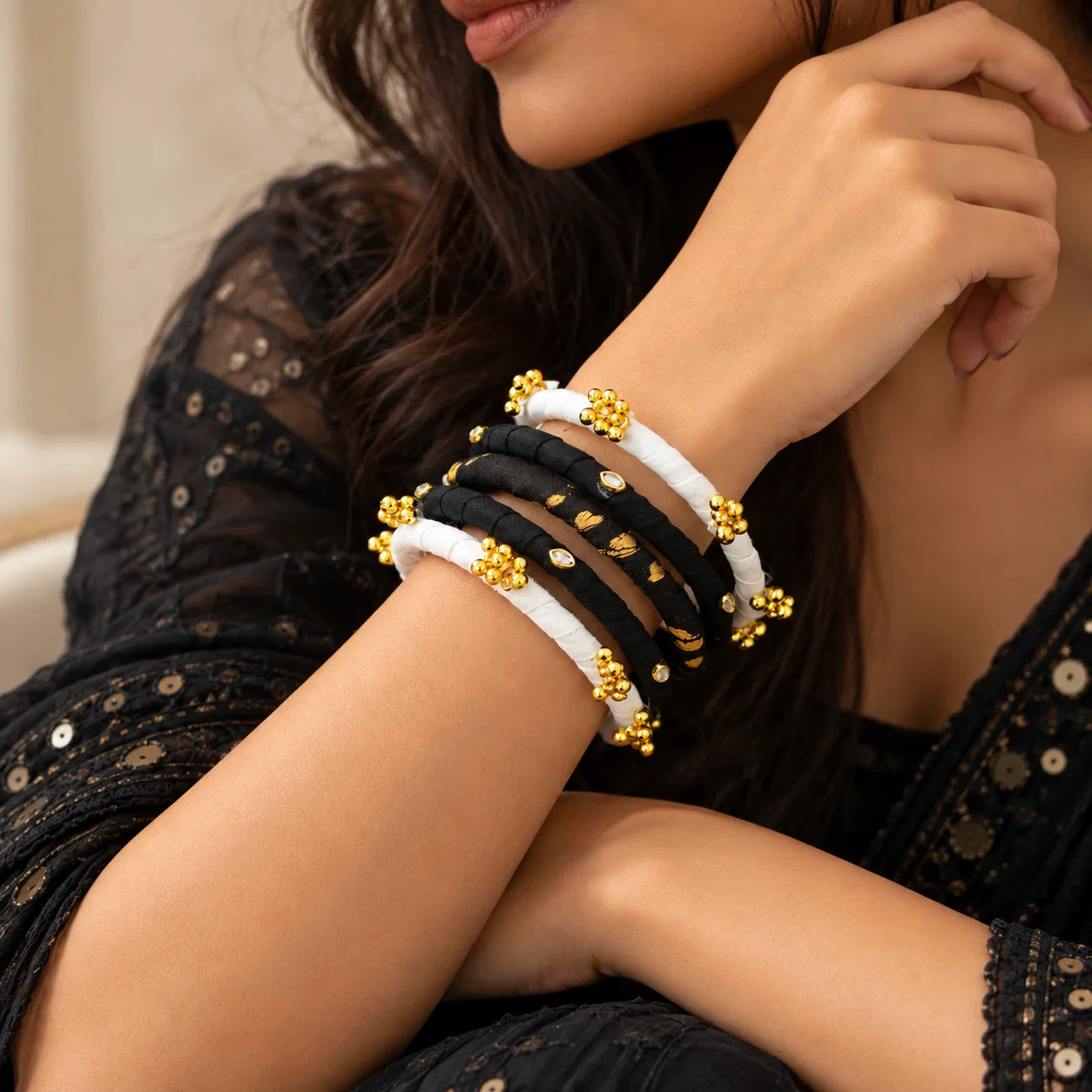 "Black and White fabric 
wrapped bangle set with Golden Ghungroo accent. Pair these bangles
 with a black saree, an ivory kurta, or a gold-accented festive outfit for a sophisticated finish."
