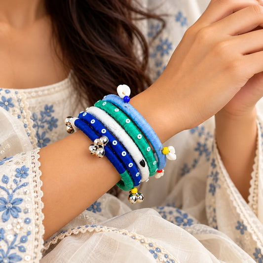 "Multicoloured fabric-wrapped
 bangle set in blue, green, white, and navy, featuring dotted patterns, colourful beads, white drop-shaped charms, and silver-tone bells , perfect for indo-western look."
