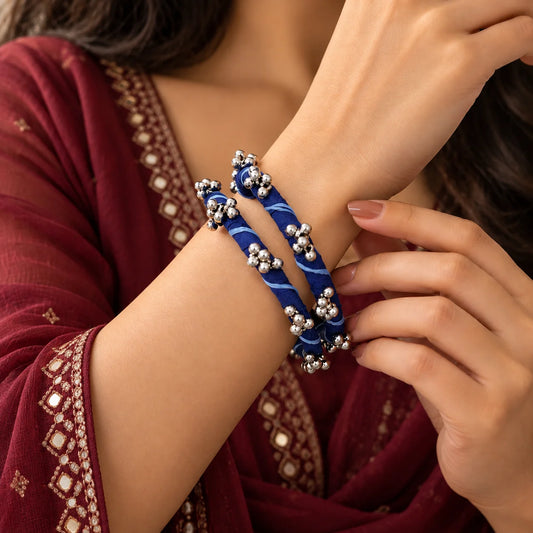 "Royal blue fabric-wrapped 
bangle set featuring delicate white swirl patterns and silver-tone bead cluster embellishments, worn on the wrist."
