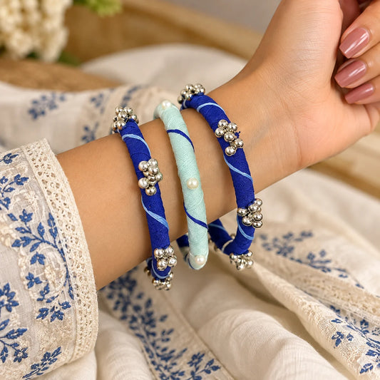 "Deep blue and
sky blue fabric-wrapped bangle set featuring white swirl patterns and silver-tone bead cluster embellishments, worn on the wrist."
