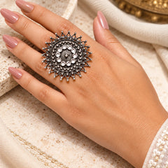 "Oxidised silver statement 
ring featuring an intricate circular design, concentric embossed patterns, and decorative sunburst edges with delicate bead-like accents."
