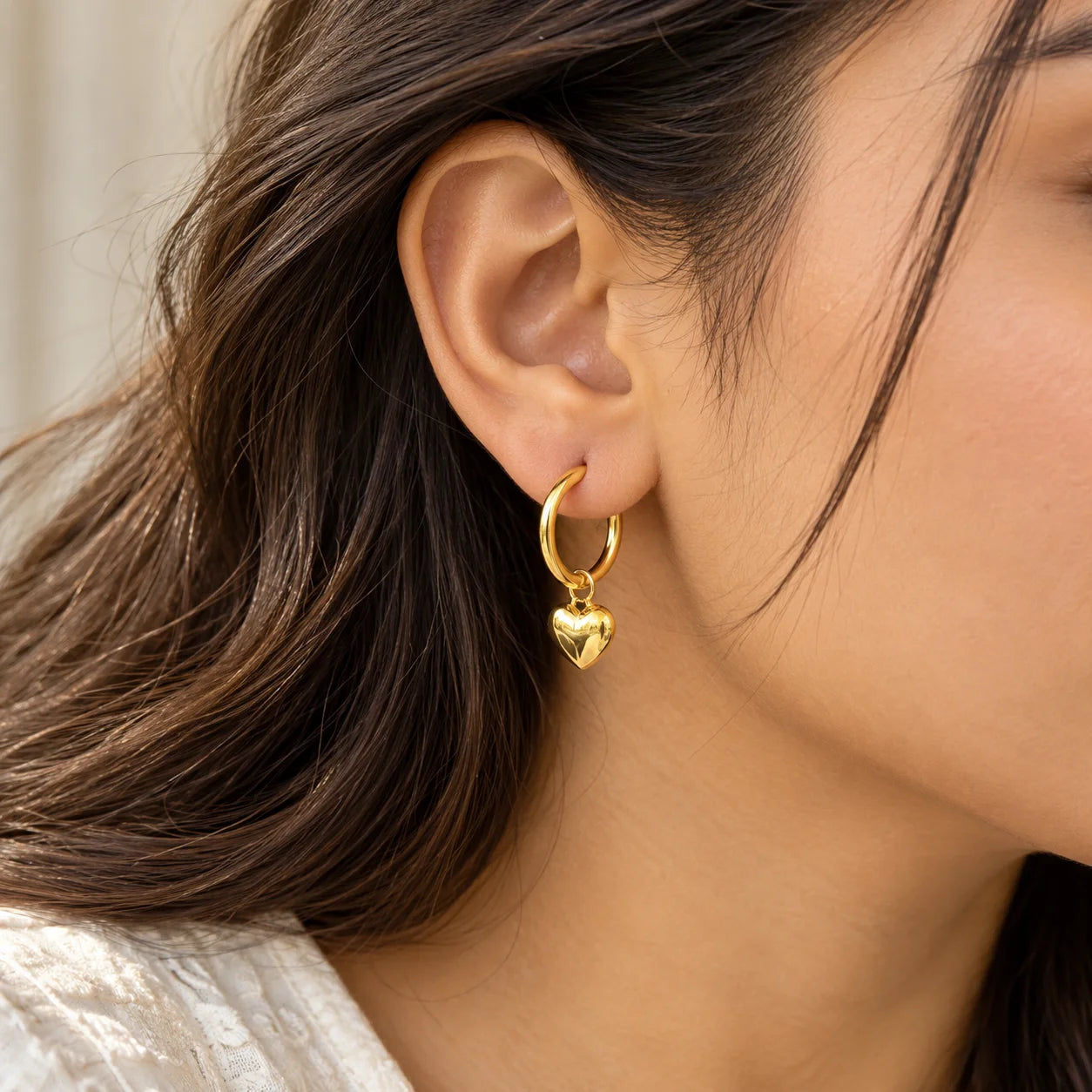 Gold hoop earrings with dangling heart charms and a polished finish, photographed on a neutral background.

