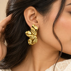 Gold sculpted leaf drop earrings featuring a wavy, textured design and a polished metallic finish.
