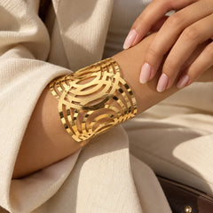 Gold-tone geometric hand cuff bracelet featuring multiple curved, layered bands with cutout detailing and a polished metallic finish.

