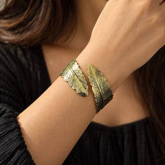 Antique gold-tone open cuff bracelet featuring textured feather motifs and detailed engraved lines.
