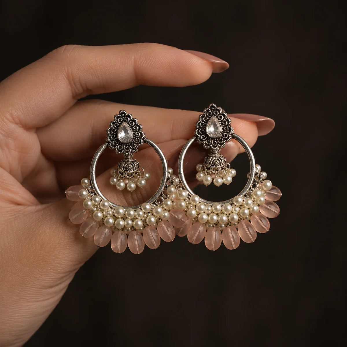 Silver plated chandbali jhumka earrings with baby pink beads and pearl clusters on wood. Traditional kundan stud earrings with hoop, mini jhumka, and pink bead drops for women. Festive wear silver tone chandbali earrings with white pearls and pastel pink detailing.

