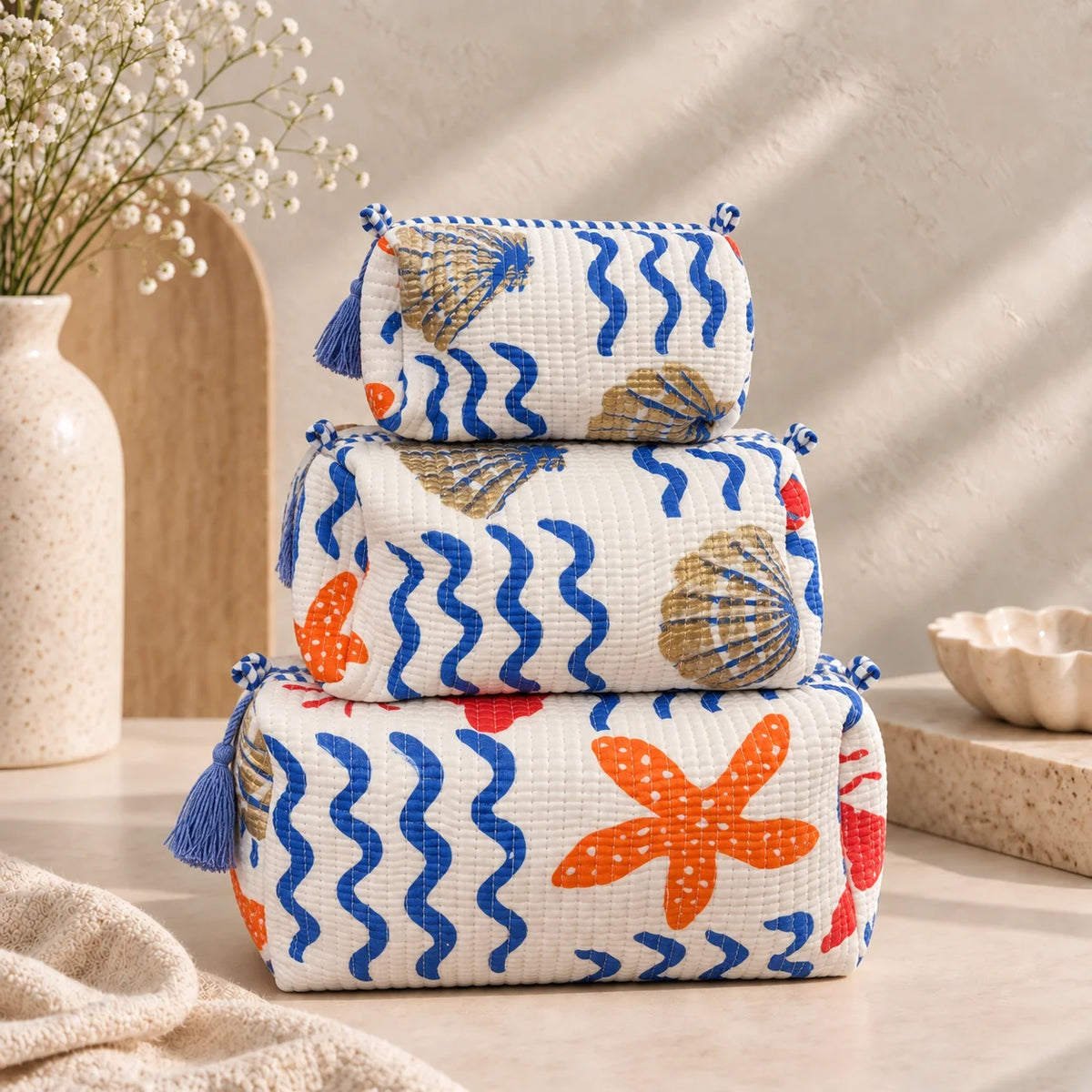 "Set of three quilted 
fabric pouch bags featuring blue wave patterns with orange,  and gold accents, finished with decorative tassels and displayed stacked together."

