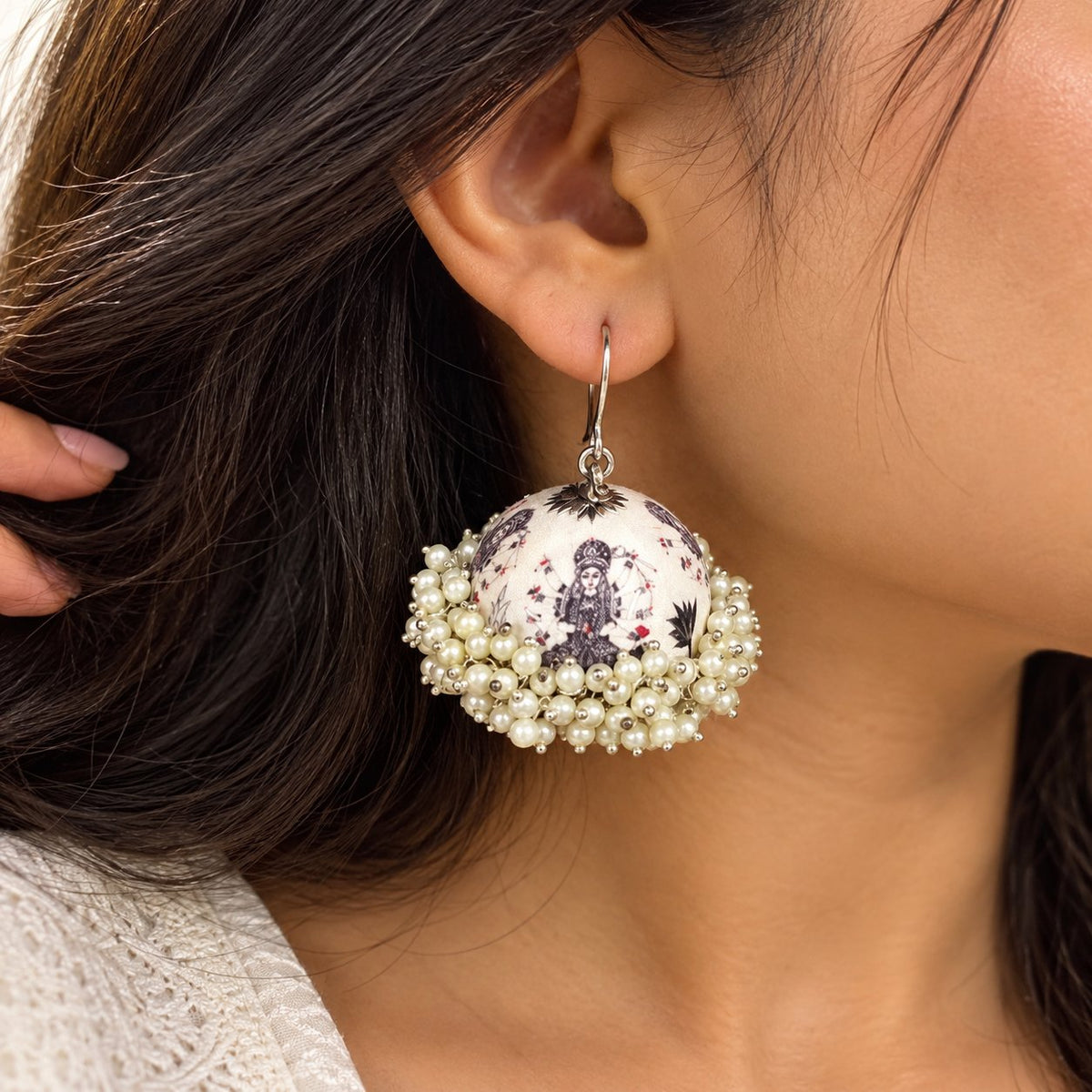 White dome-shaped Meenakari jhumka earrings featuring goddess motifs, pearl embellishments, and silver-tone hooks.
