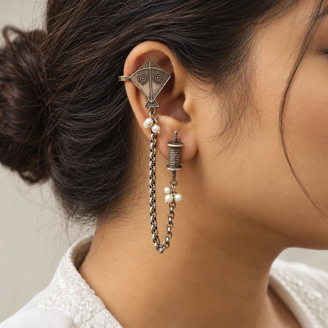 "Silver-toned statement
 earring with a geometric kite-shaped centerpiece, small pearl accents, and a long linked chain drop."
