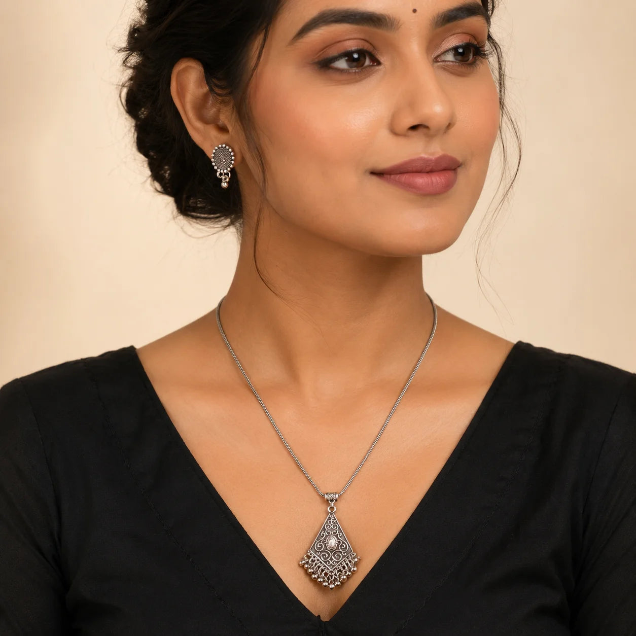 "Oxidised silver-tone necklace 
and earrings set featuring an intricate triangular pendant with ghungroo-style danglers and matching ethnic stud earrings."
