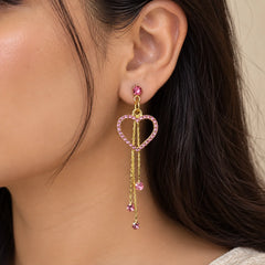 "Pair of delicate
 gold-toned dangle earrings featuring pink crystal-studded heart-shaped hoops, slender chain drops, and small pink gemstone accents."
