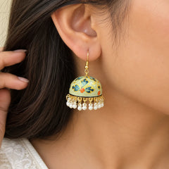"Sage-green dome-shaped
 jhumka earrings with blue floral and gold detailing, finished with white pearl-like bead danglers."
