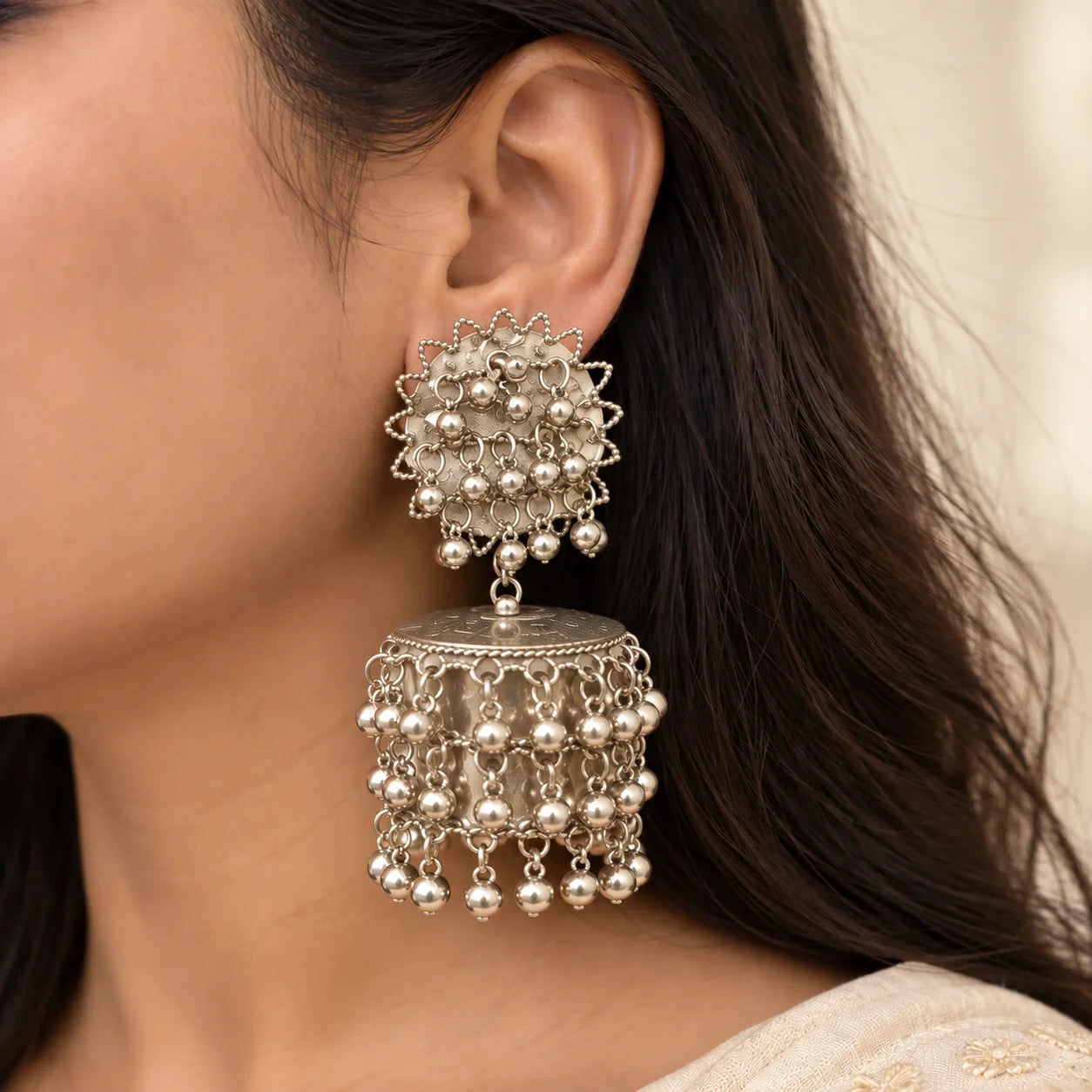 "Pair of silver-toned
 statement jhumka earrings featuring intricate textured dome designs and multiple layers of dangling ghungroo-style beads."
