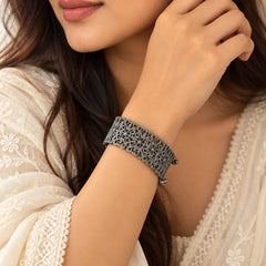 "Dark oxidised statement
 bracelet featuring intricate openwork floral filigree detailing and delicate dangling bead accents along the edges."
