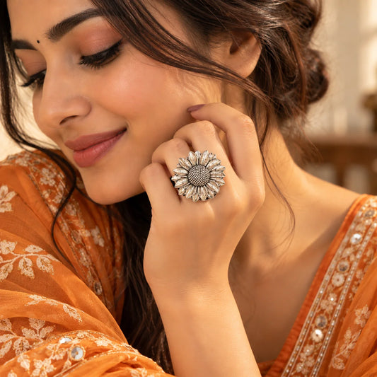 "Silver-toned statement
 ring featuring a large sunflower-inspired flower with a textured centre and layered, sculpted petals."
