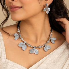 "Silver-toned necklace
 set featuring intricate leaf-inspired motifs arranged along the necklace, paired with matching leafy earrings."
