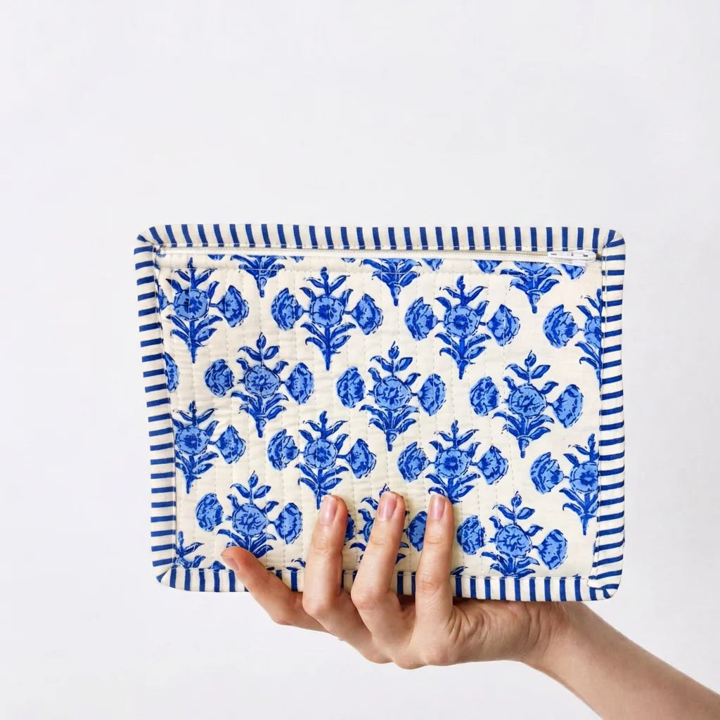 "Blue and white quilted
 fabric pouch featuring a repeating floral print and striped border detailing."
