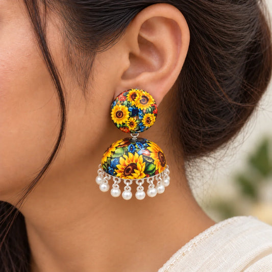 "Colorful floral jhumka
 earrings featuring vibrant yellow sunflowers, multicolored flowers, and green foliage on a dark background, finished with white bead danglers."
