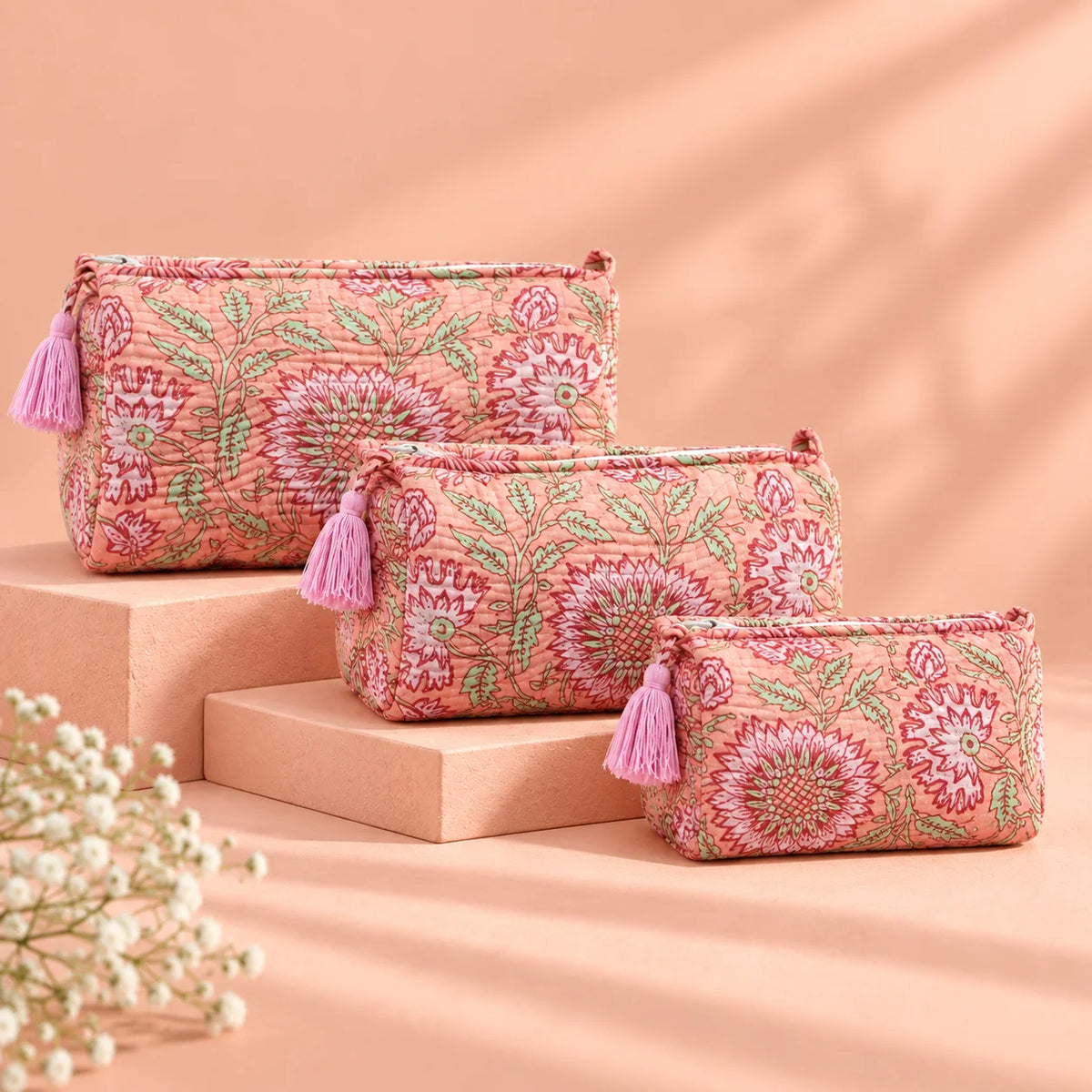 "Set of three peach
 fabric pouches featuring intricate floral and leafy prints in burgundy, rose, and green, arranged in different sizes."
