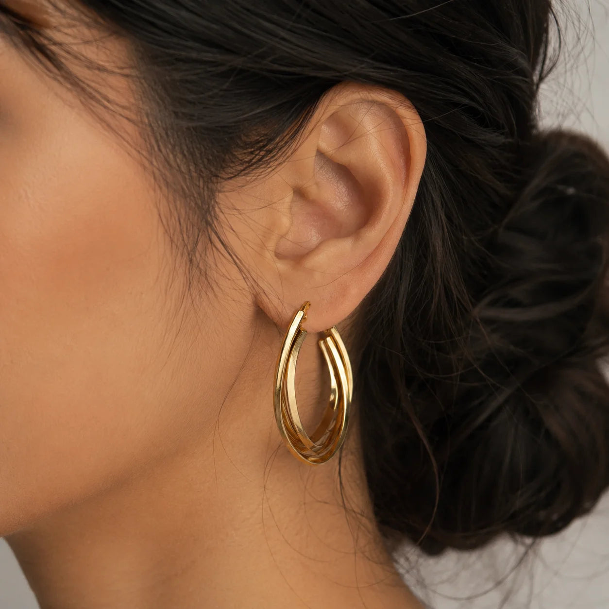 Gold double layer oval hoop earrings on wooden surface. Pair of gold-tone twisted hoop earrings with latch-back closure.
