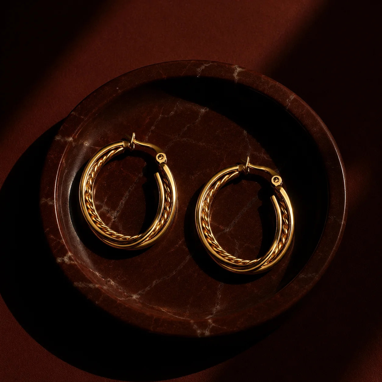 Hand holding gold triple layer hoop earrings with braided chain detail. Large gold-tone hoop earrings featuring three rows and rope texture center.
