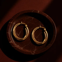 Hand holding gold triple layer hoop earrings with braided chain detail. Large gold-tone hoop earrings featuring three rows and rope texture center.
