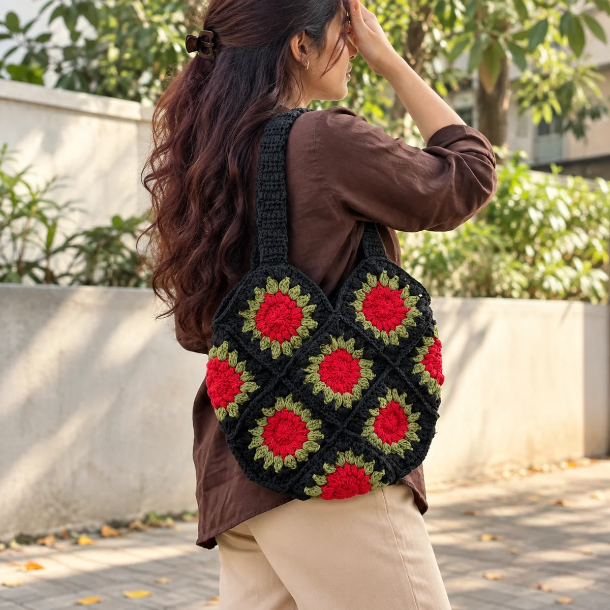 "Handcrafted black crochet
 bag featuring bold red floral motifs with olive-green leaf detailing and sturdy crochet handles."

