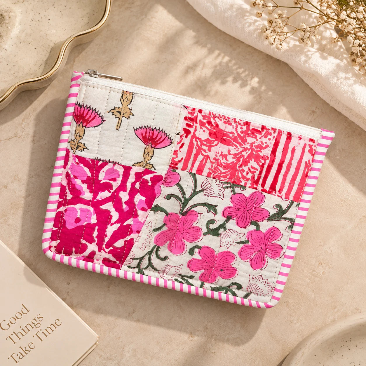 "Pink and white quilted 
patchwork pouch featuring floral and botanical prints, a striped border, and a zip closure."
