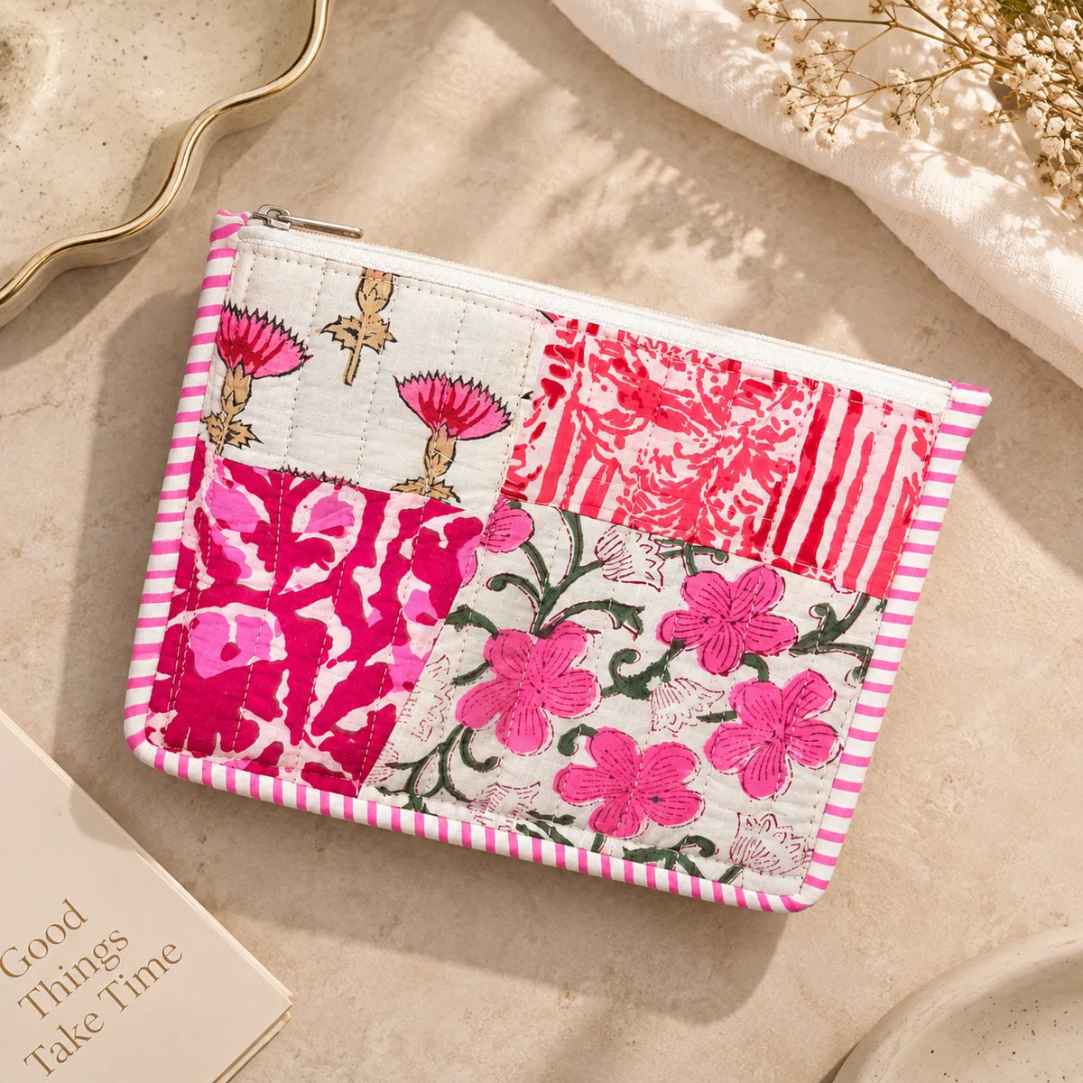"Pink and white quilted 
patchwork pouch featuring floral and botanical prints, a striped border, and a zip closure."
